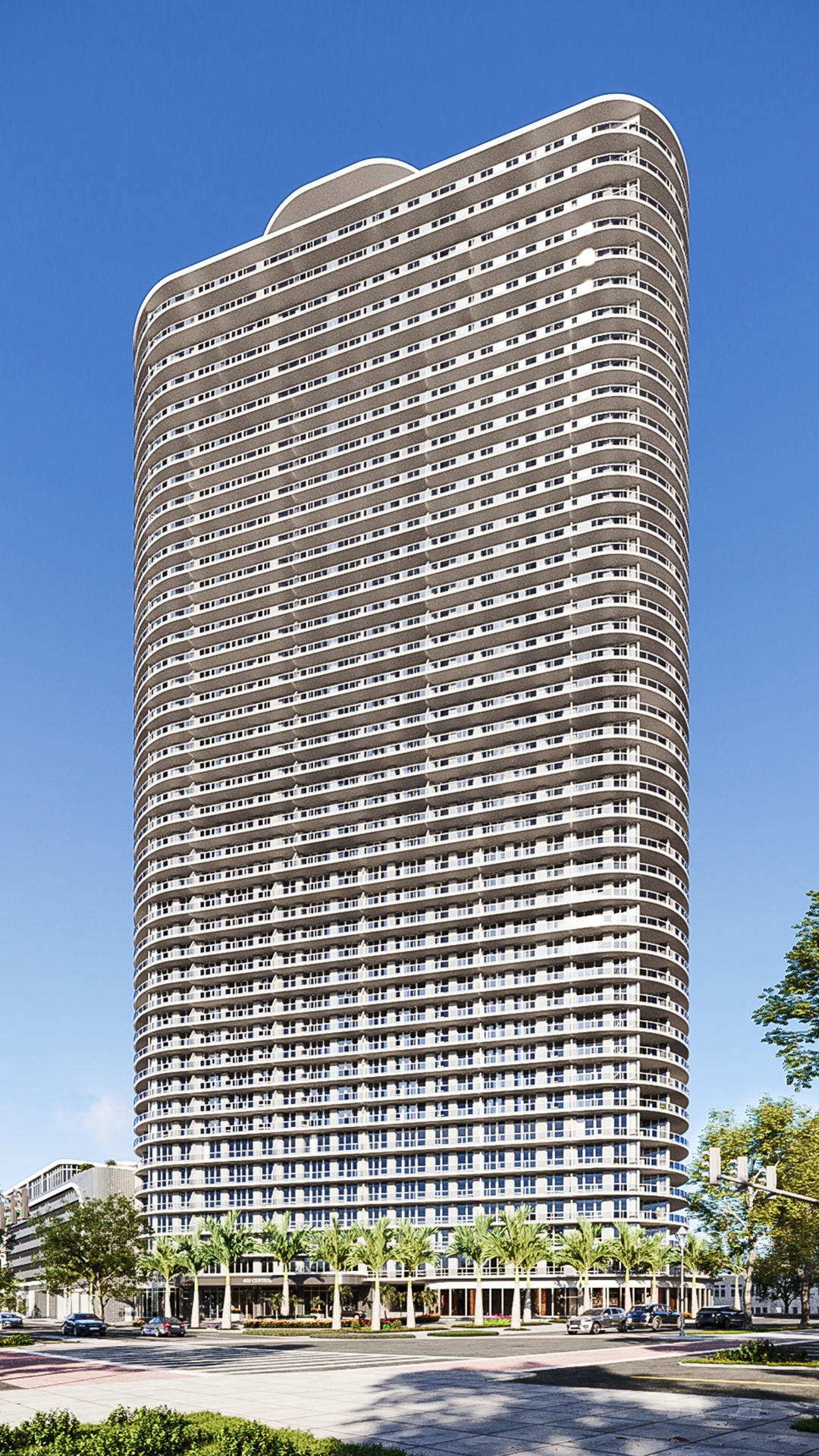 A tall, modern residential high-rise with rounded corners and numerous balconies stands against a clear blue sky, with trees and a street visible at the base.