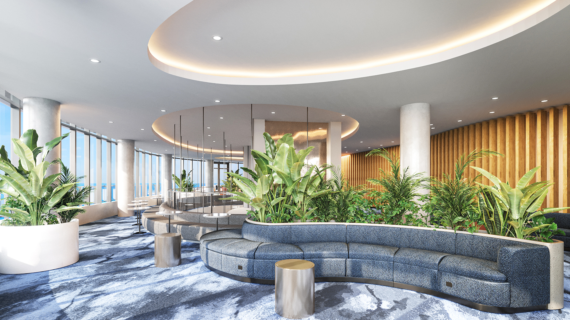 A modern, residential lounge with curved blue seating, round gold tables, lush green plants, large windows offering city views, and a ceiling with soft recessed lighting.