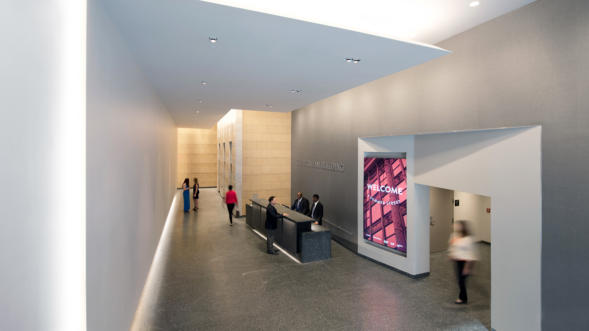 Modern building lobby with a reception desk, people walking and talking, a large digital welcome screen on the wall, and stylish light gray walls with recessed lighting—perfect for retail spaces seeking a welcoming atmosphere.
