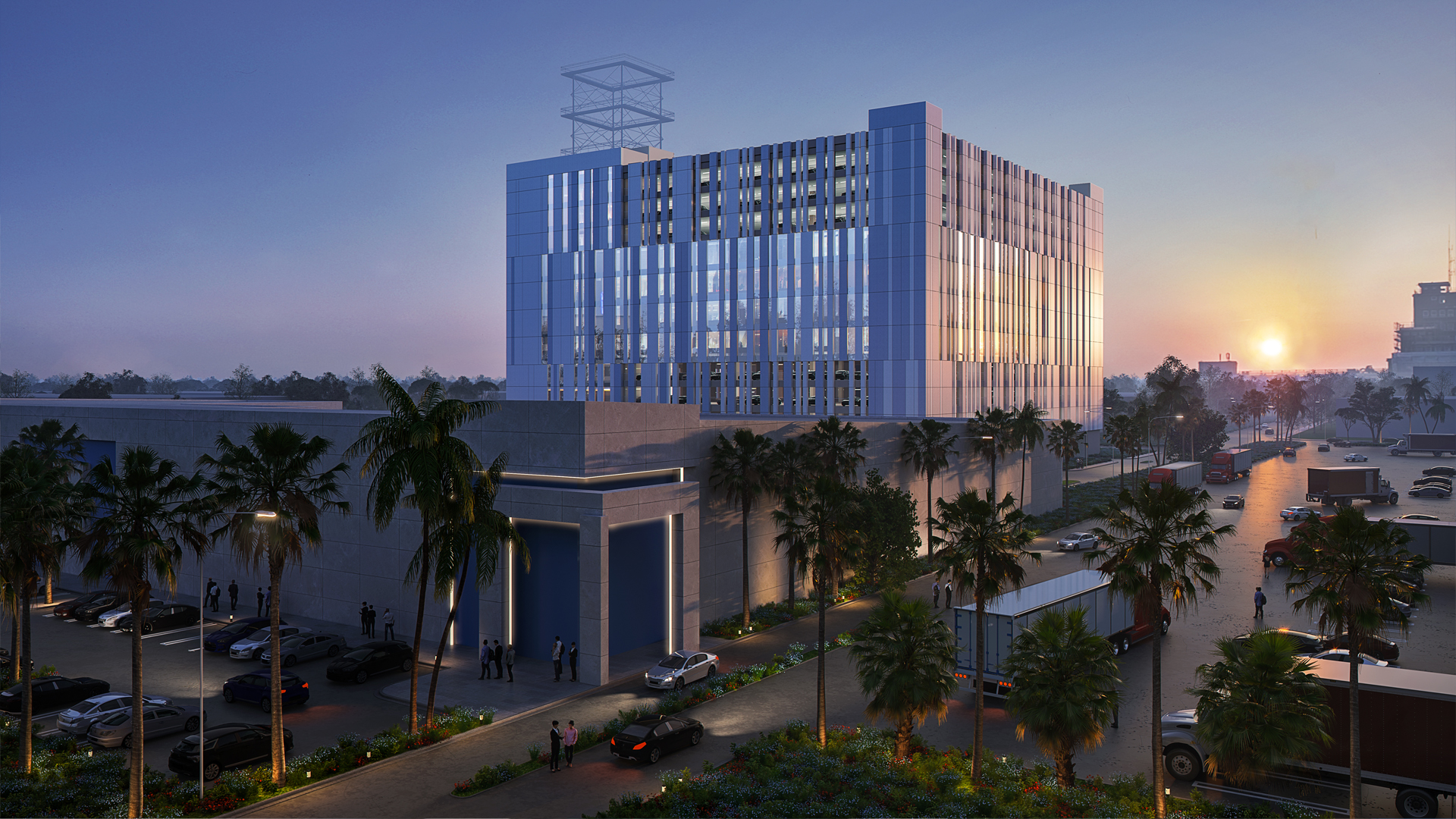 A modern, multi-story Federal Government building with reflective glass windows at sunset, surrounded by palm trees, parked cars, and trucks, set along a landscaped street with people walking nearby.