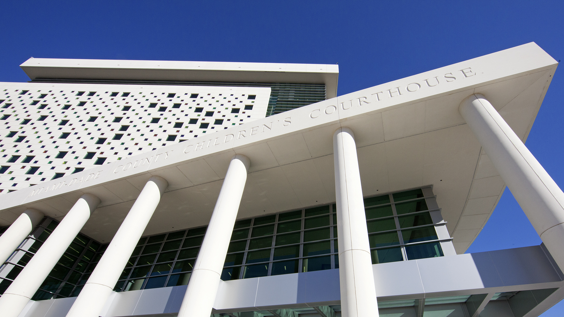 Modern courthouse building with tall white pillars and geometric windows, featuring a section labeled Children’s Courthouse. This Federal Government facility stands tall against a clear blue sky.
