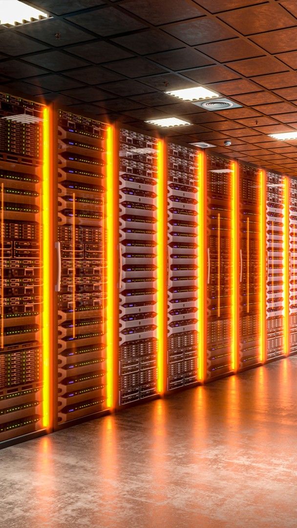A modern, mission critical server room with rows of server racks illuminated by vertical orange LED lights, reflecting on a polished floor and a dark tiled ceiling above.