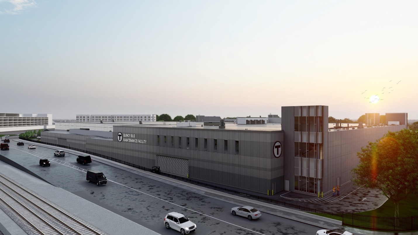 A modern, gray transportation facility with “MBTA” signage is shown at sunrise. Cars drive on the adjacent road, and train tracks run parallel to the building. Trees and parked vehicles are visible nearby.