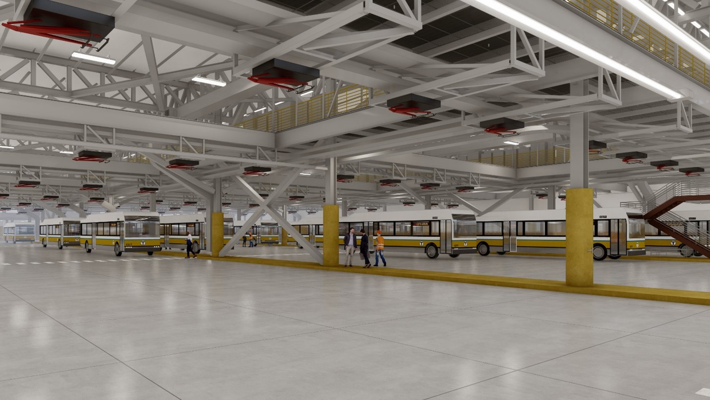 Interior of a large, modern bus depot with white beams, yellow columns, and a row of yellow and white buses parked. Several people in safety vests walk near the buses on the spacious concrete floor.
