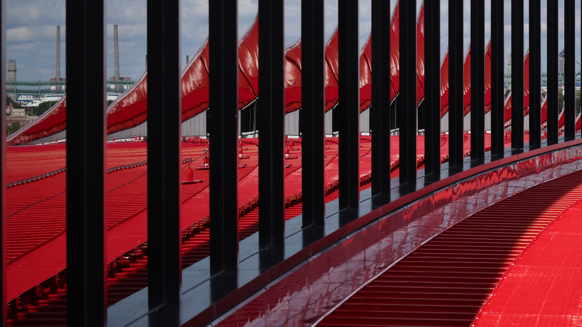 Rows of vertical black bars and bright red angled panels create a striking geometric pattern, evoking themes of aviation & transportation, with industrial buildings and smokestacks blurred in the distant background.