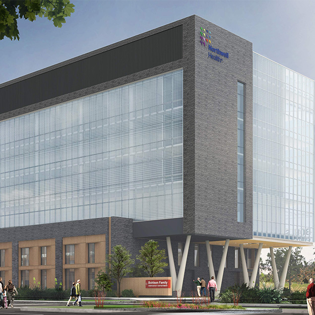 A modern multi-story hospital building with large glass windows and the Northwest Health logo. People walk along the sidewalk in front, and there are trees and landscaping near the entrance.