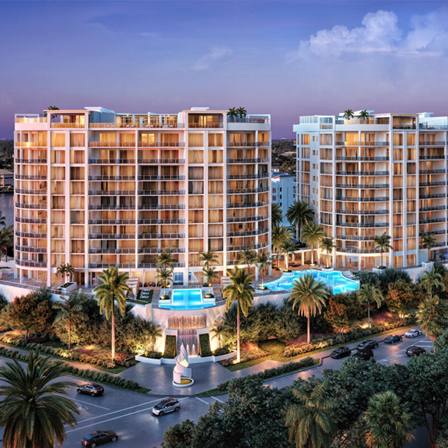 Two modern, mid-rise apartment buildings with large balconies are illuminated at dusk. Palm trees and landscaped gardens surround the pools and the entrance, while cars pass by on nearby roads.