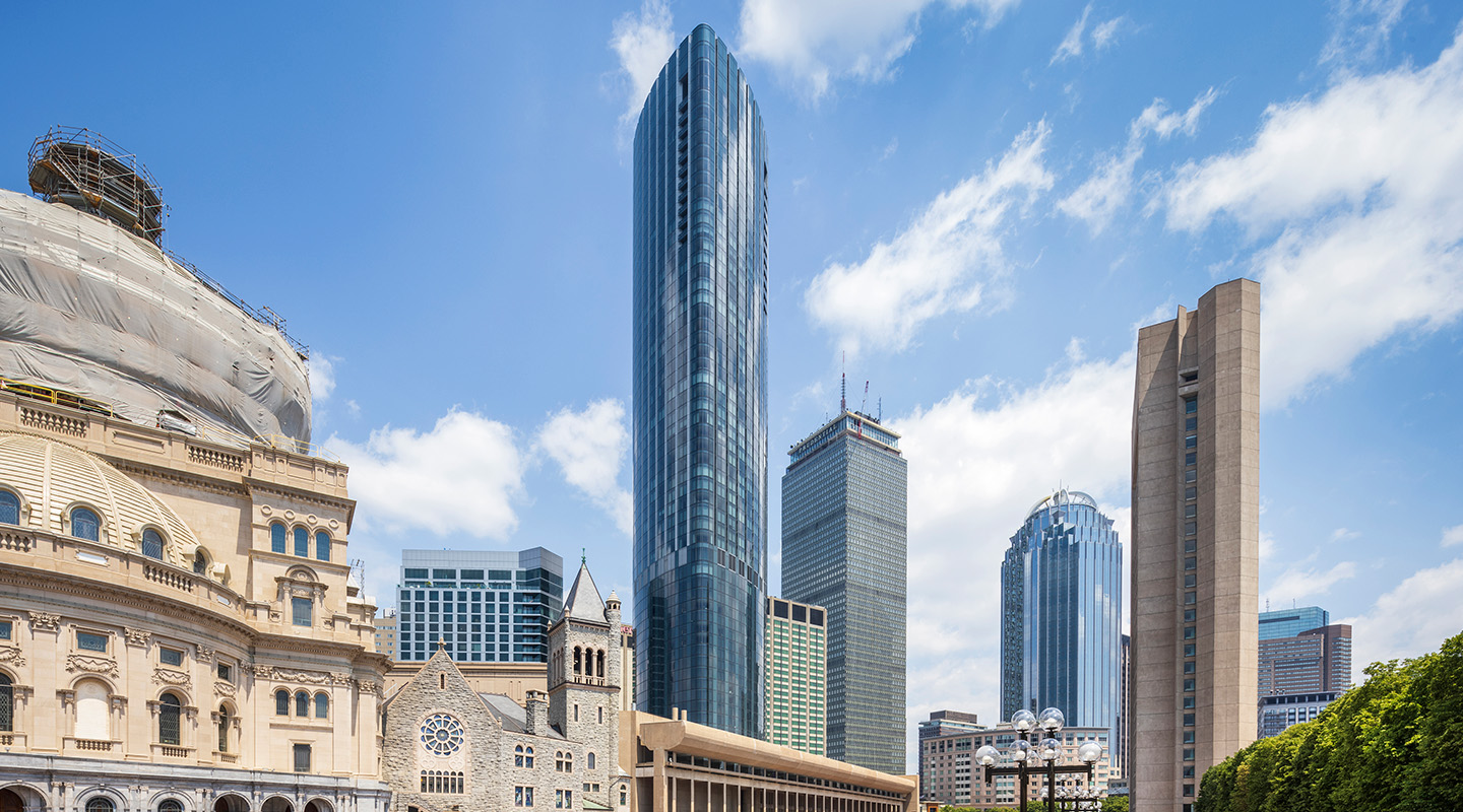 A cityscape view of Boston featuring modern skyscrapers, including a tall glass building, historic stone churches on the left, and a blue sky with scattered clouds in the background.