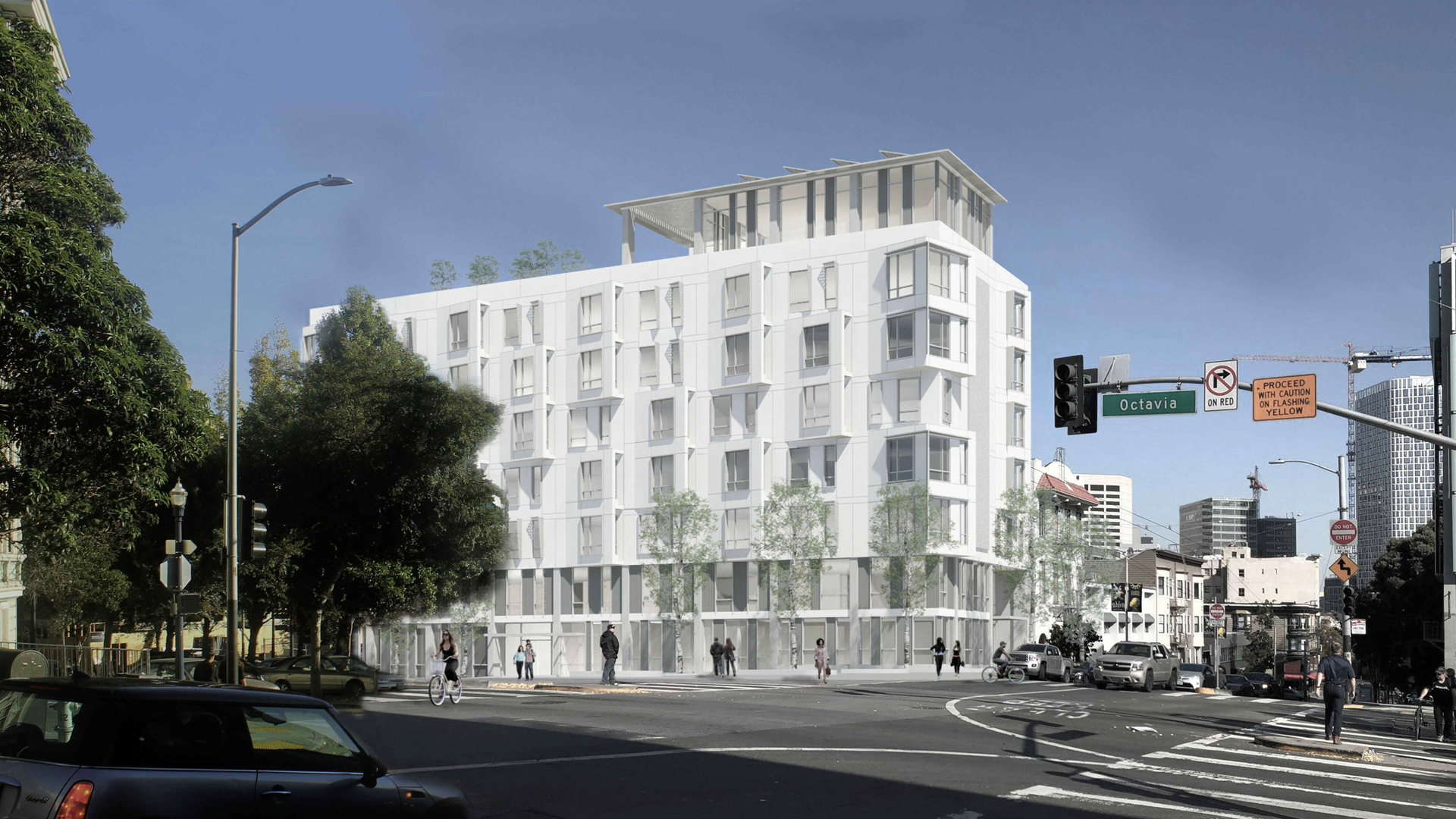 A modern, white multi-story apartment building with large windows stands at a city intersection with traffic signals, trees, pedestrians, and parked cars under a clear blue sky.