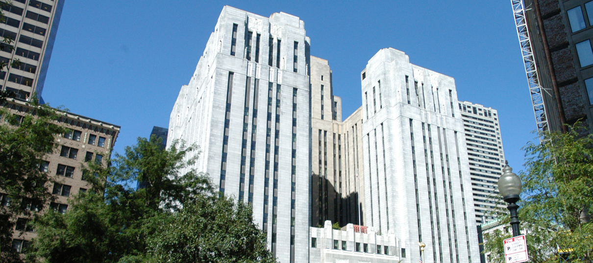 Tall, art deco-style hospital building with white stone exterior and vertical lines, surrounded by trees and other high-rise buildings under a clear blue sky.