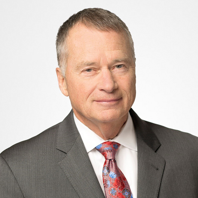 A middle-aged man with short gray hair, wearing a gray suit, white shirt, and a colorful patterned tie, poses against a plain light background—an ideal portrait for an Advisory Board member.