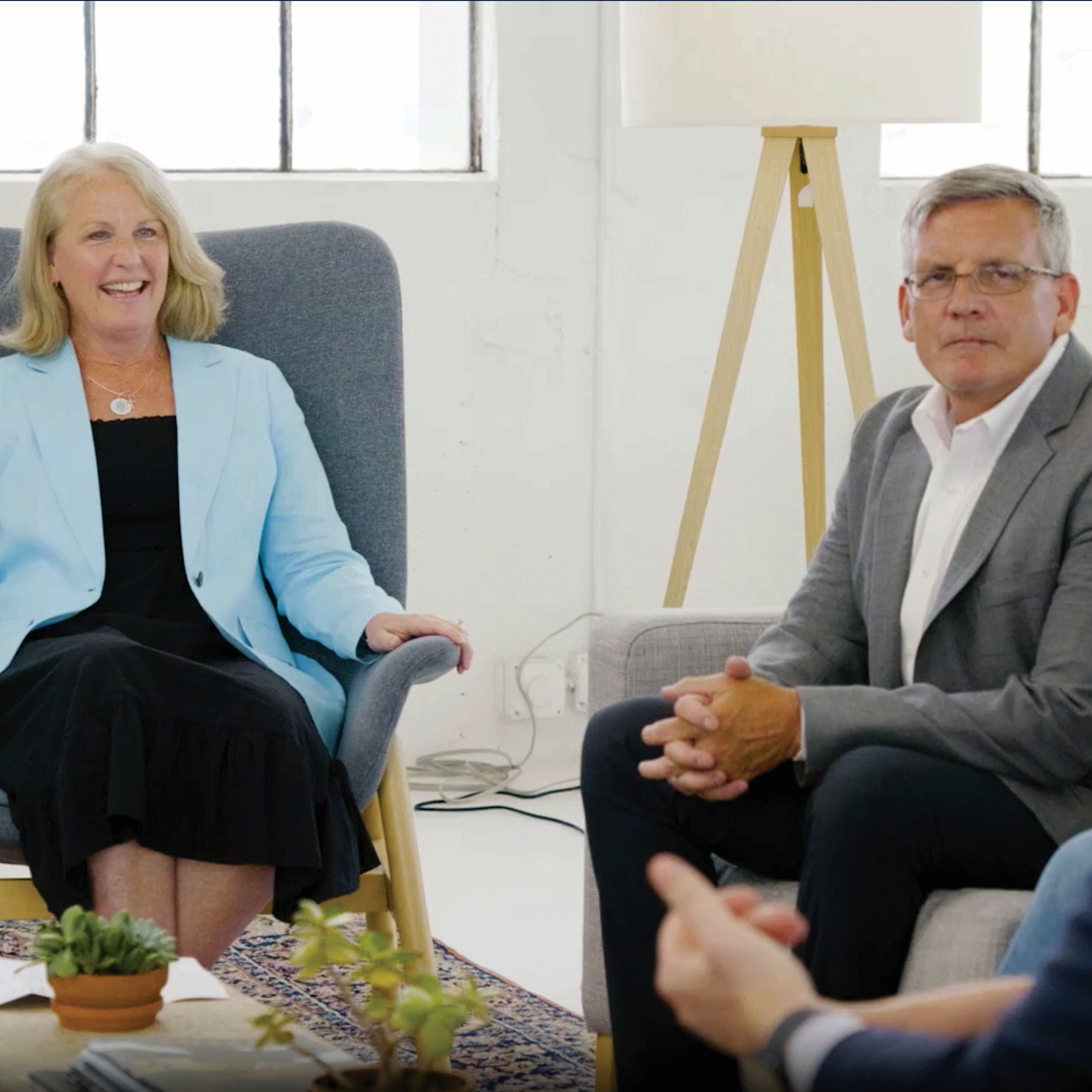photo of a man and a woman sitting in a chair with work clothes on one is smiling one is listening to someone off camera