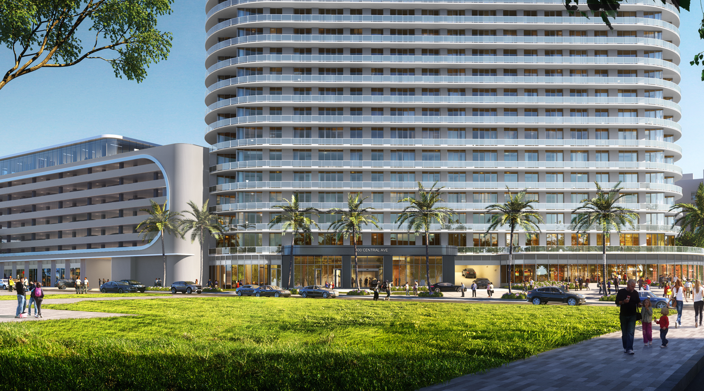 A modern, multi-story hotel with curved balconies and glass windows stands behind a green lawn, palm trees, and several people walking or standing. Cars are parked and driving in front of the main entrance.