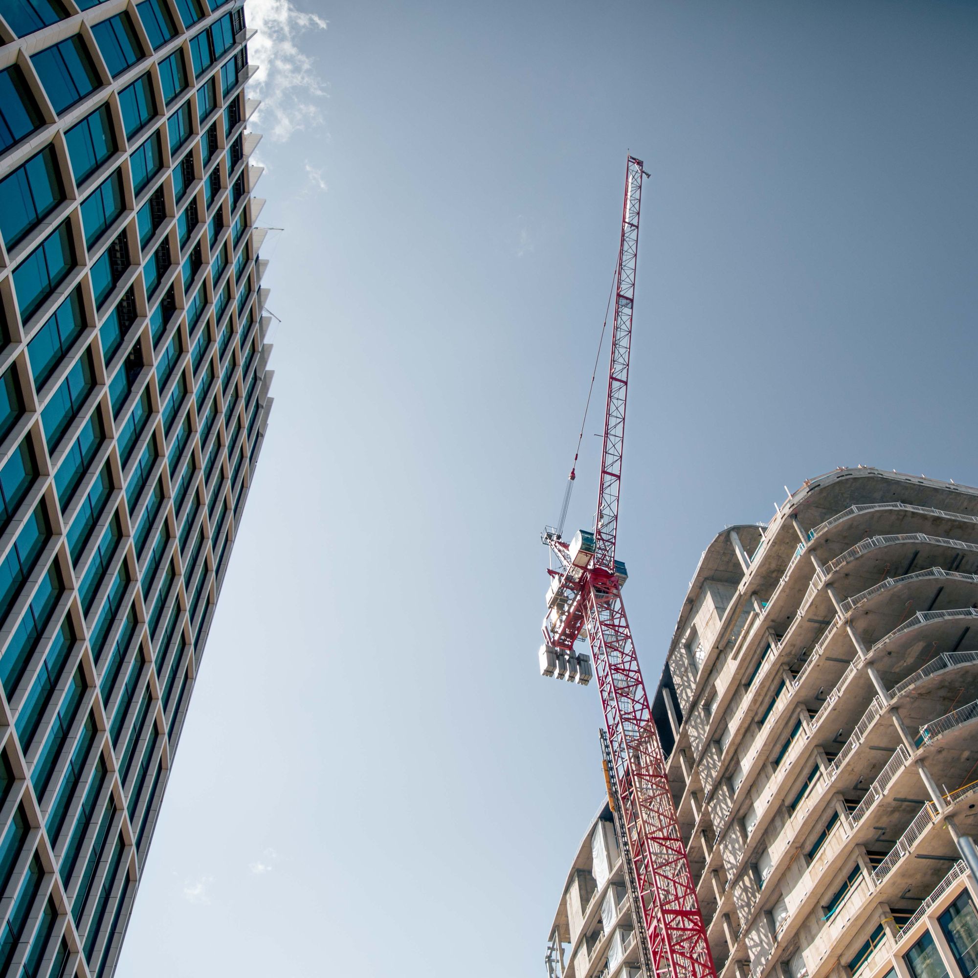 looking up at two skyscrapers one with a crane blue sky in background
