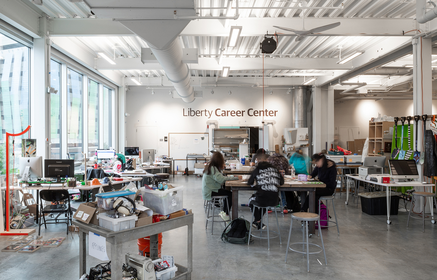 A spacious, modern classroom labeled Liberty Career Center with students working at tables, computers, and various technical equipment in a bright, open environment with large windows.
