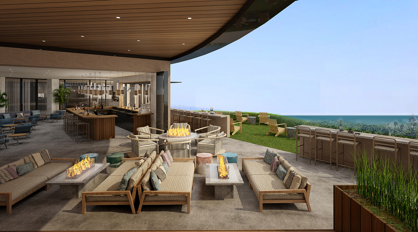 Modern outdoor lounge with cushioned sofas around fire pits, overlooking a grassy area and ocean view. Indoors, a bar and seating area are visible under a curved wooden ceiling.
