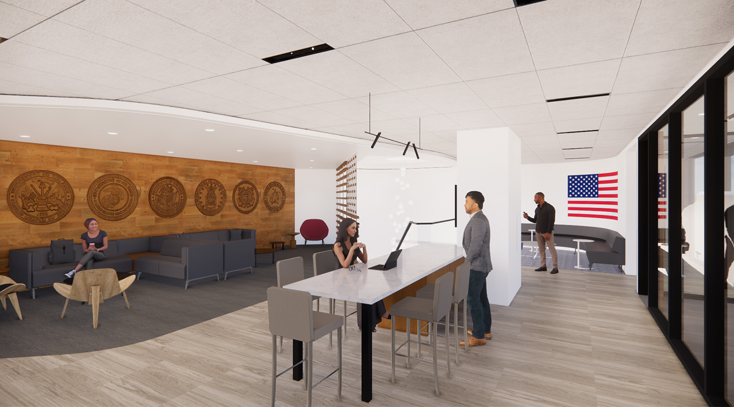 A modern office space with people working and talking. There are couches, a long table, and an American flag on the wall. Military emblems are displayed on a wooden accent wall in the background.