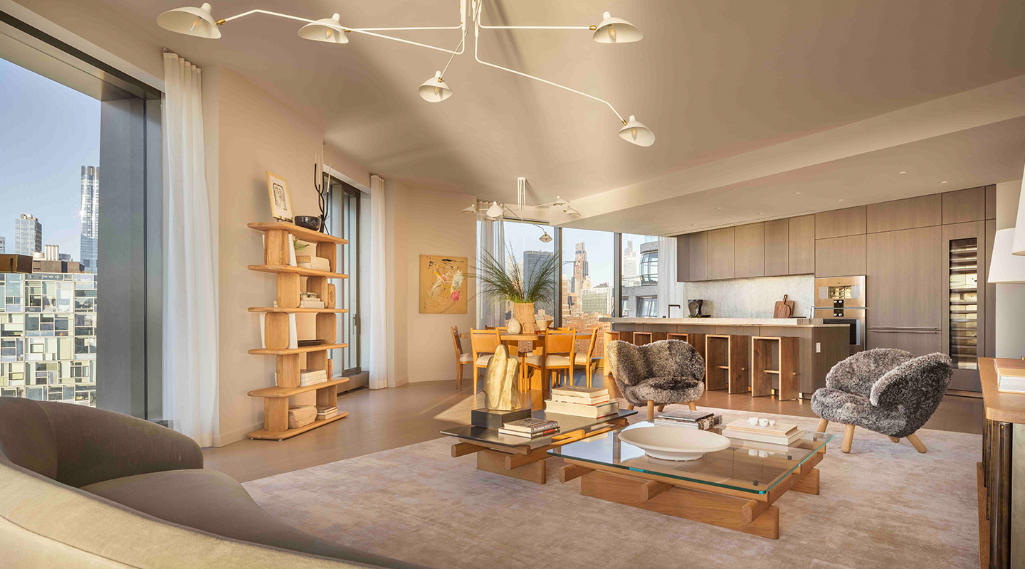 A modern, sunlit open-plan living and dining area with floor-to-ceiling windows, city views, neutral tones, cozy armchairs, a wooden dining table, and a minimalist kitchen with sleek cabinets in the background.
