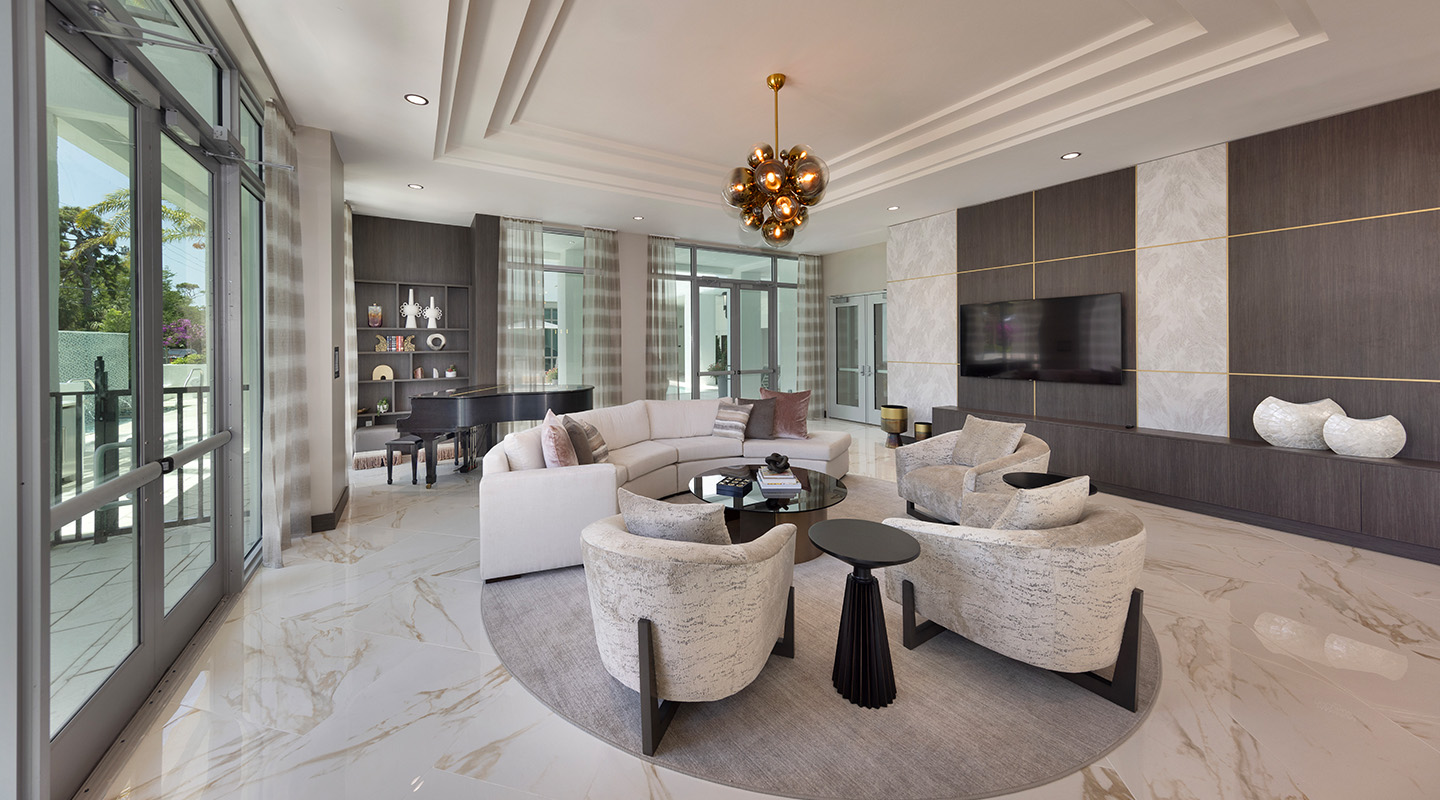 Modern living room with marble floors, a round white sofa, two armchairs, a black coffee table, wall-mounted TV, accent shelves, large windows, and a grand piano. Gold and wood accents give a luxurious, airy feel.