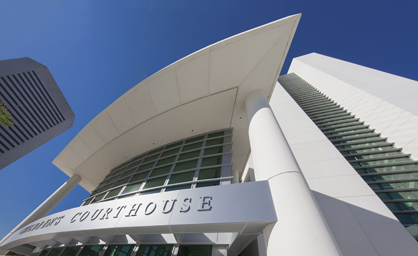 A modern courthouse building with tall white columns, large glass windows, and a curved roof, photographed from a low angle against a clear blue sky.