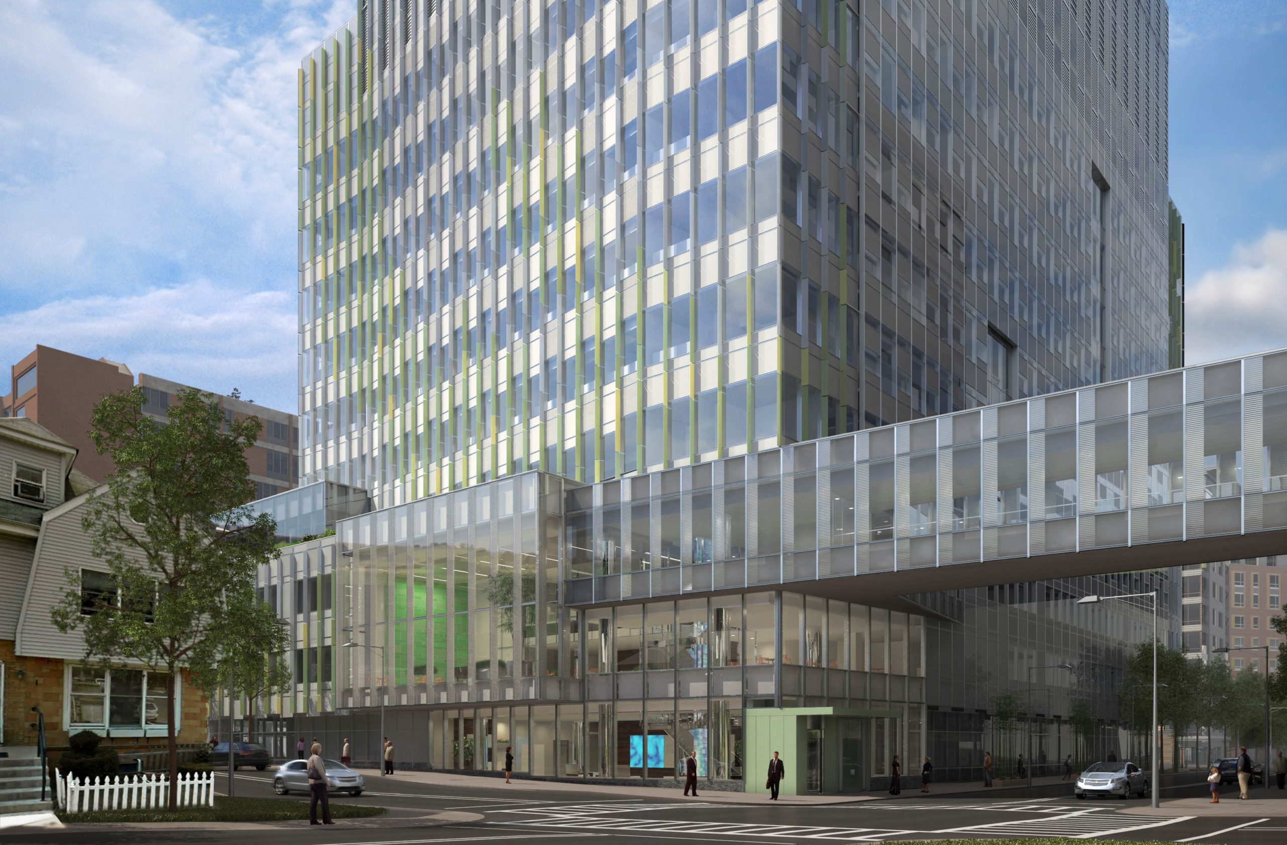 A modern glass office building with green accents stands on a city street corner, connected by a glass skywalk to another building. Cars and pedestrians are visible nearby.
