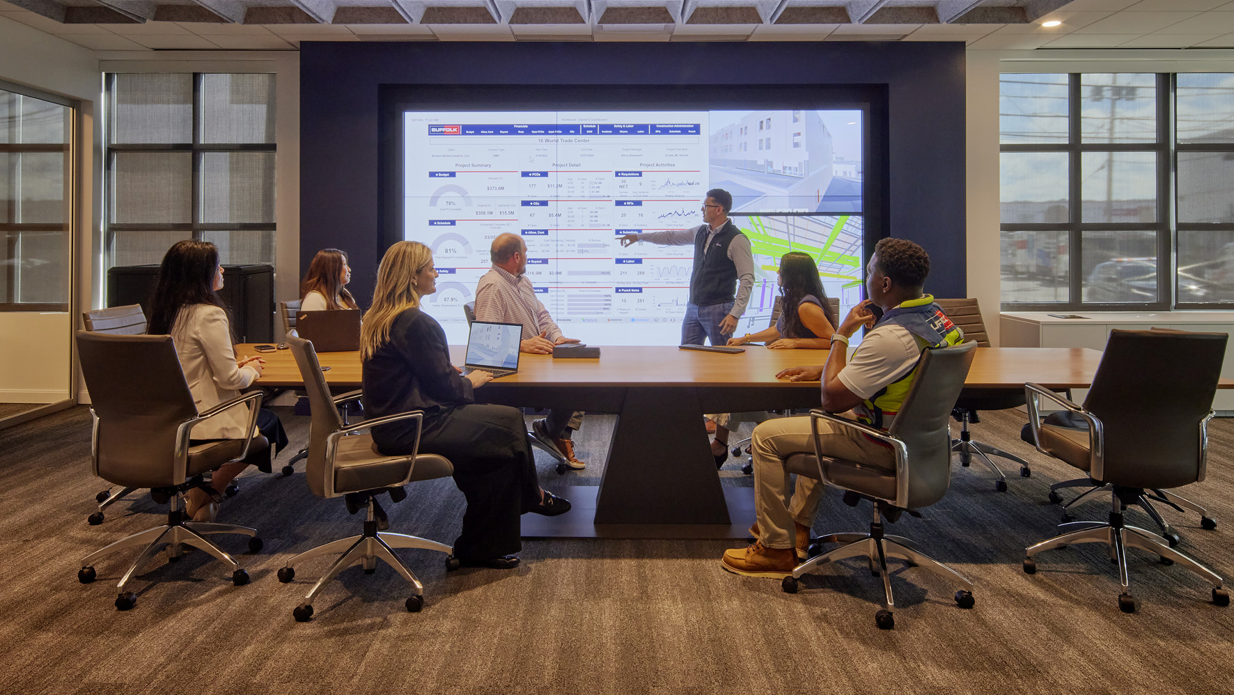 people in board room pointing at monitor with data
