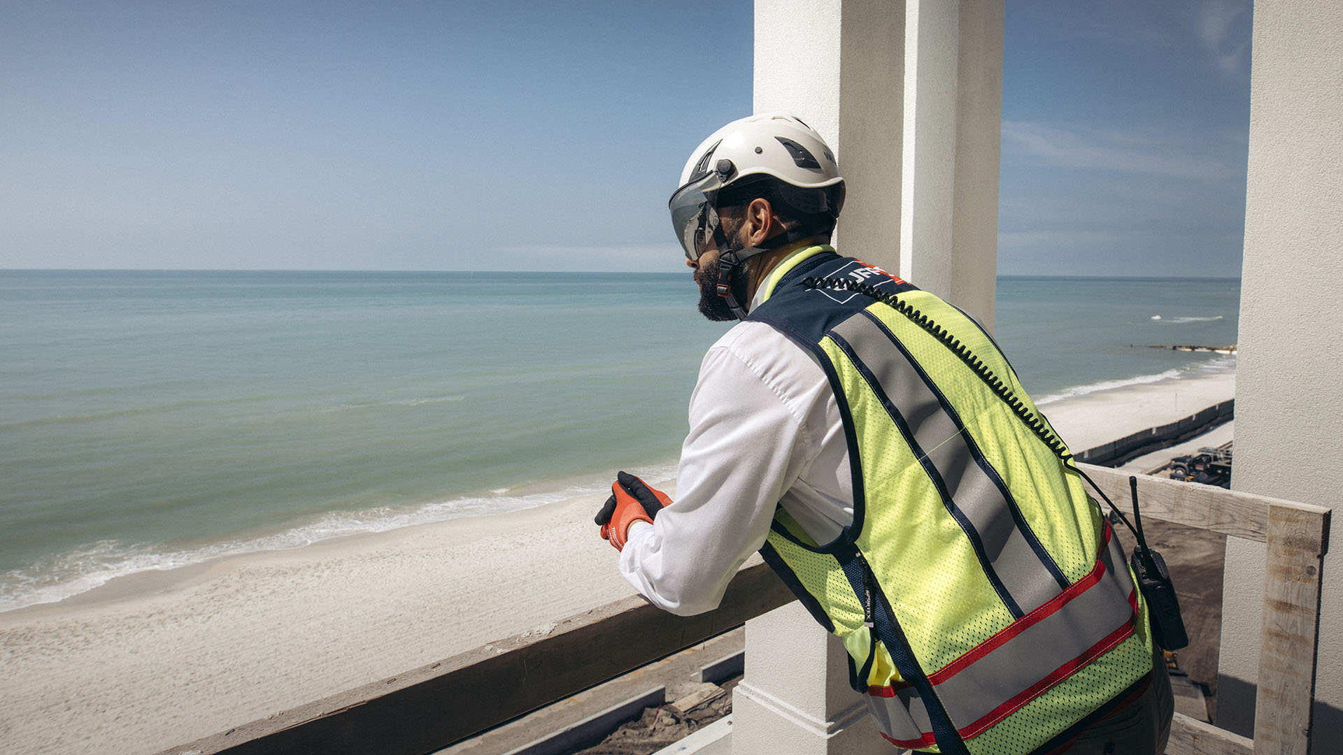 construction worker looking out into the distance with full gear on near beach