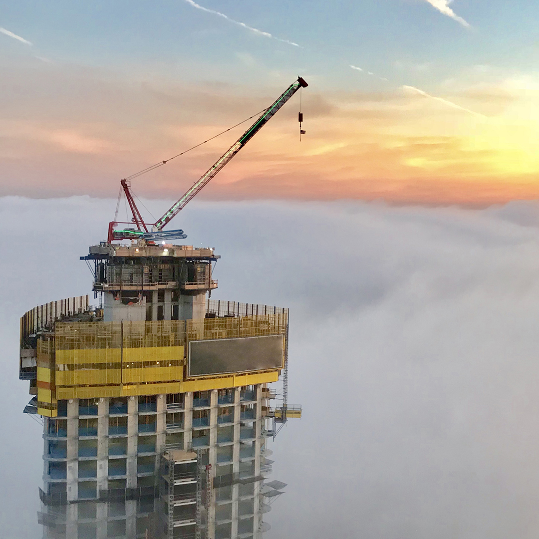 aerial photo of office building under construction with crane on top in the clouds with sun setting