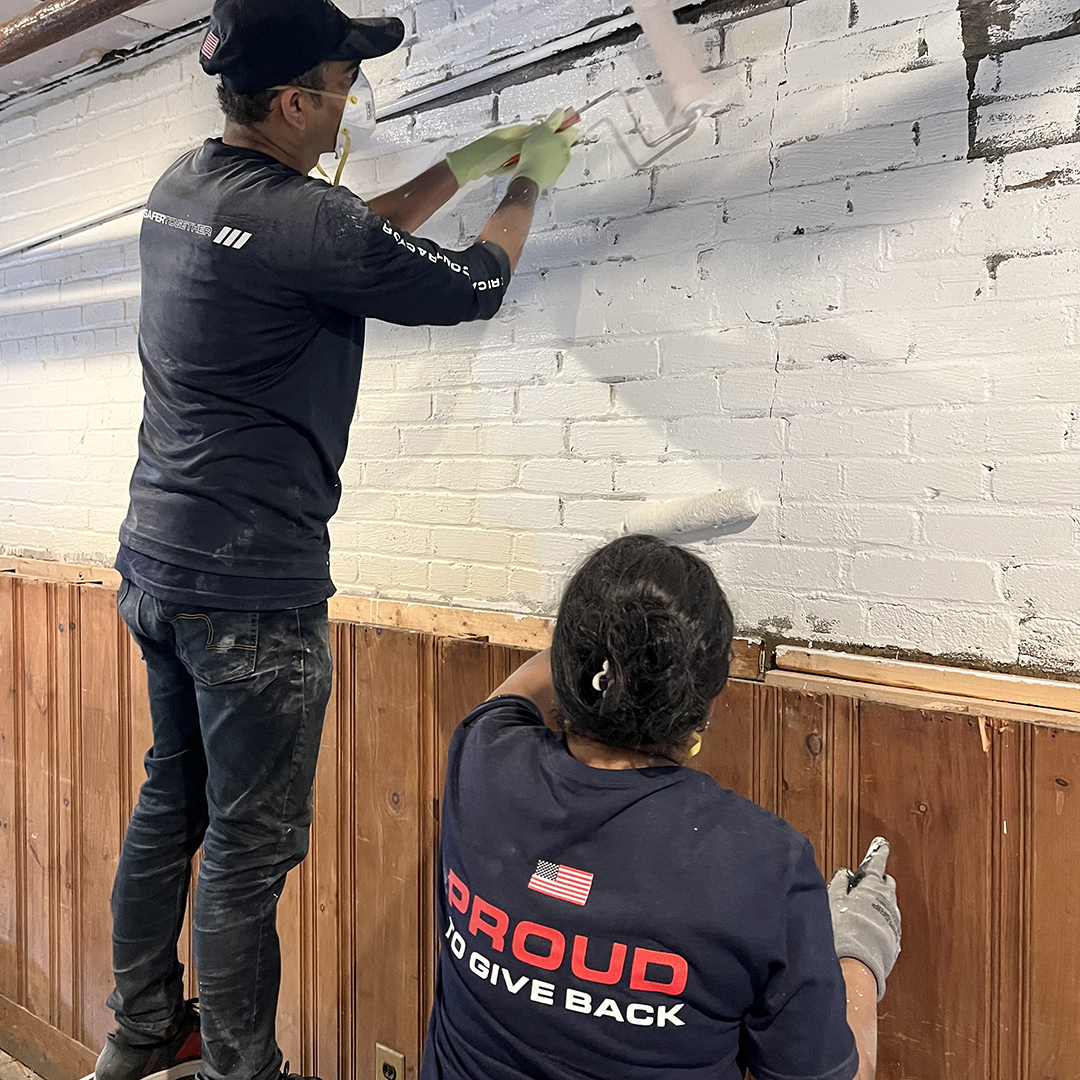 2 people in proud to give back shirts helping painting a wall