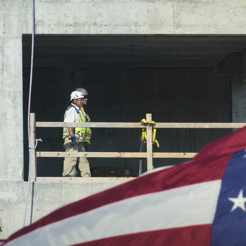 A construction worker in a safety vest and helmet stands on a concrete building site, demonstrating The Suffolk System’s commitment to safety, with part of an American flag visible in the foreground.