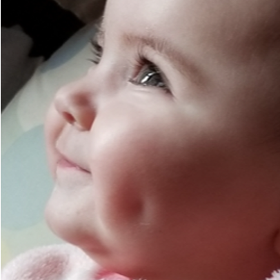A close-up side profile of a smiling baby with rosy cheeks, deep dimples, and bright eyes, looking upward. The baby is wearing a light pink outfit.